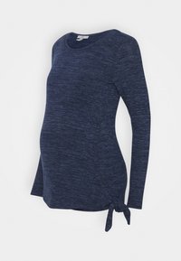 Haut de maternité bleu marine à manches longues en tissu doux et texturé, avec un détail nœud sur le côté et un ourlet arrondi pour une coupe décontractée.