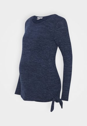 Haut de maternité bleu marine à manches longues en tissu doux et texturé, avec un détail nœud sur le côté et un ourlet arrondi pour une coupe décontractée.