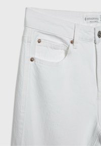 Jeans in denim bianco con una finitura texturizzata. Presentano una tasca anteriore con un accento di rivetto in metallo e un'etichetta tradizionale in vita.