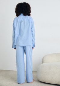 Blårandig pyjamasset gjort av lättviktigt tyg. Innehåller en knapplöst skjorta med långa ärmar och matchande löst sittande byxor.