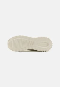 Såle av en sneakers i off-white gummi, med en teksturert overflate med horisontale riller og sirkulære mønstre for godt grep.