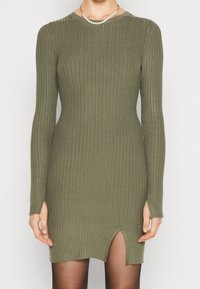 Robe en tricot côtelé vert olive à manches longues, avec un décolleté en forme de bateau et une fente sur le devant près de l'ourlet. Texture lisse, design près du corps.
