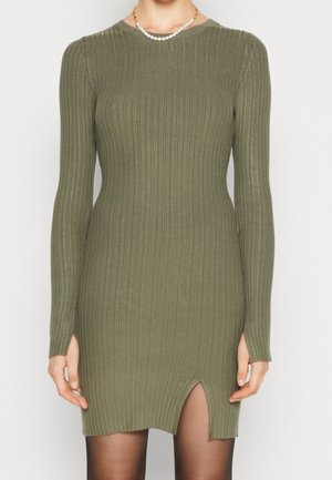 Robe en tricot côtelé vert olive à manches longues, avec un décolleté en forme de bateau et une fente sur le devant près de l'ourlet. Texture lisse, design près du corps.