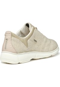Zapatillas de tela beige con un upper texturizado, acentos de color rosa claro en contraste y una suela de goma blanca acolchada. Presenta un detalle del logo.
