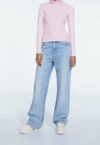 Svetle růžový žebrovaný rolák v kombinaci s volnými světle modrými džíny. Model má na sobě robustní bílé tenisky. Jednoduchý, moderní design.