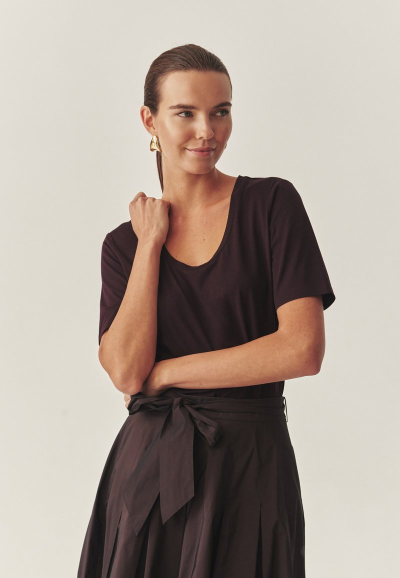 Czarny t-shirt z okrągłym dekoltem w połączeniu z czarną spódnicą o wysokim stanie, która ma kokardkę. Tkanina wydaje się gładka i miękko opada.