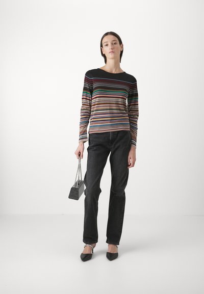 Top de manga larga a rayas con finas rayas de colores, combinado con unos jeans de mezclilla negros, y sosteniendo un pequeño bolso gris con una correa de cadena.