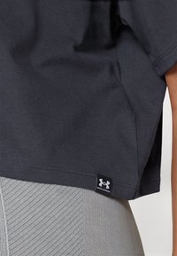 Dark gray cotton t-shirt with a loose fit, short sleeves, and a stitched hem. Features a small black Under Armour logo tag on the side.