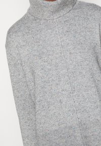 Lichtgrijze gebreide trui met multikleurige spikkels, voorzien van een hoge ribbelkraag en een centrale verticale naden detail.