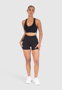 Reggiseno sportivo nero e pantaloni corti a vita alta abbinati, realizzati in tessuto elastico. L'outfit presenta un collo a barca e una vestibilità aderente.