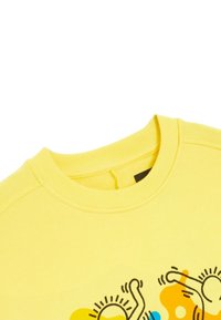 Felpa gialla in cotone con colletto a coste e un design grafico giocoso di forme astratte in blu e arancione.