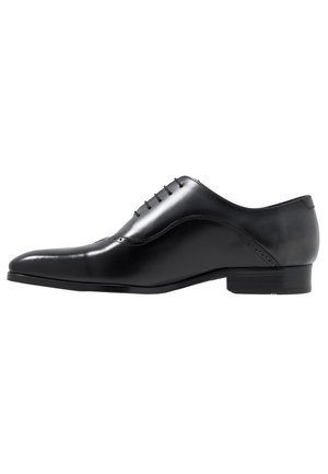 Chaussure de ville Oxford en cuir noir avec laçage fermé, bout pointu, talon bas et détails brogue subtils sur le côté.