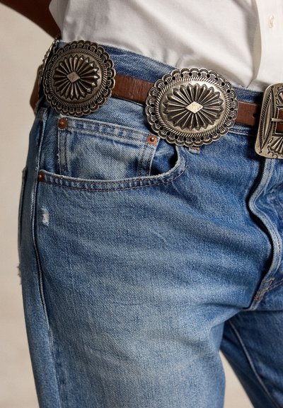 Modré denimové džíny nošené s hnědým koženým páskem s velkými stříbrnými ozdobnými přezkami ve stylu concho.