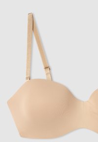 Reggiseno beige senza cuciture con tessuto morbido, coppe modellate e spalline sottili e regolabili in satin. Presenta una leggera lucentezza e una chiusura a gancio.