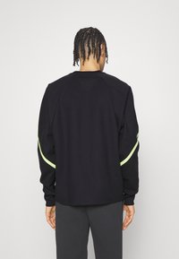 Felpa nera a maniche lunghe con vestibilità rilassata, con una striscia verde fluorescente lungo le maniche e un colletto a girocollo.