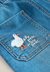 Farkkutasku, jossa valkoinen kirjailtu ankka oranssilla nokalla ja jaloilla, teksti "silly goose in the house" sinisellä kankaalla.