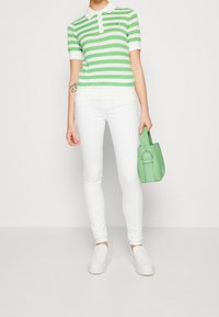 Camisa polo a rayas verdes y blancas, jeans ajustados blancos, zapatos blancos sin cordones y un pequeño bolso verde con un acento de hebilla.