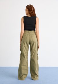 Groene cargo pants met een hoge taille, wijde pijpen en meerdere cargopockets; katoenen materiaal met een gladde textuur. Zwarte tanktop.