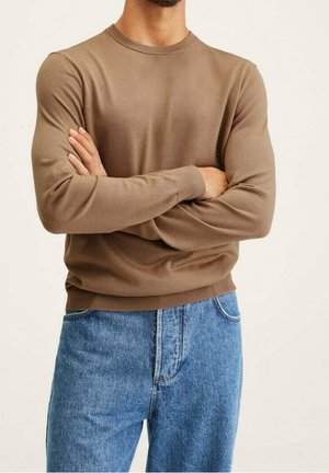 Langer brauner Pullover mit Rundhalsausschnitt aus weichem Stoff, kombiniert mit hellblauen geraden Jeans. Der Stoff wirkt glatt und hat eingesetzte Ärmel.