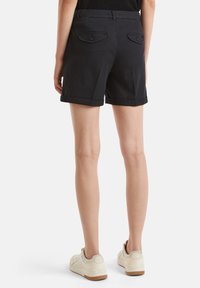 Černé bavlněné šortky s rovnými nohavicemi, ohrnutým lemem a dvěma zadními kapsami se zavíráním na knoflíky. Nahoře má světle barevné tenisky.