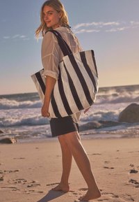 Gestreepte tote bag in zwart-wit stof, met brede handvatten. De tas heeft een rechthoekige vorm en een licht gestructureerd oppervlak.