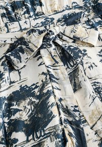 Rochie dintr-un material moale, cu un model abstract în nuanțe de albastru, negru și bej. Include un detaliu cu talie legată și un design fluid.