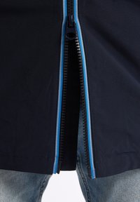 Granatowa kurtka z kontrastowym niebieskim zamkiem, charakteryzująca się gładką teksturą materiału i otwartym przodem, w zestawieniu z jasnoniebieskimi dżinsami.