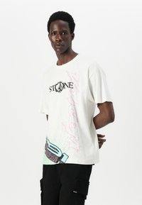Short-sleeve, cream t-shirt featuring a graphic design in pink and blue, with "STONE" printed in black across the chest.