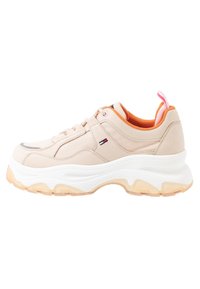 Sneaker beige con suola bianca spessa, tomaia testurizzata e foderatura arancione. Presenta dettagli metallici e una linguetta rosa sul tallone.