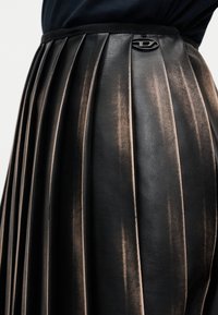 Μαύρη δερμάτινη φούστα με πιέτες και υφή, με διακριτική μεταλλική γυαλάδα και λογότυπο στη μέση.
