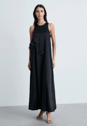 Black maxi dress with a relaxed fit, sleeveless design, and decorative black floral appliqués. Smooth, lightweight fabric, ankle-length.