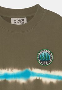 Olijfgroene sweatshirt met een geribbelde kraag, voorzien van een blauwe tie-dye streep en een ronde geborduurde patch met bomen en tekst.