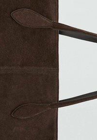 Brązowa zamszowa torba tote z dwoma długimi, płaskimi uchwytami. Charakteryzuje się gładką teksturą i minimalistycznym designem. Brak widocznych elementów metalowych lub wzorów.