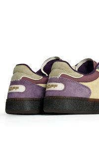 Un par de zapatillas moradas, beige y marrón con suelas negras, vistas desde la parte trasera, mostrando la marca "HOFF" en las pestañas del talón.