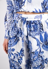 Hemd mit blau-weißer Blumenmusterung, Knopfdetails und lockerer Passform, dazu eine Hose mit gebundenem Bund aus weichem, strukturiertem Stoff.