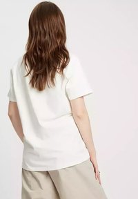 Biała, krótki rękaw t-shirt o luźnym kroju. Wykonany z miękkiej bawełny, z prostym wzorem i delikatnym opadaniem, widok z tyłu.