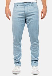 Lichtblauwe gestreepte jeans met een slim fit ontwerp, voorzien van een ritssluiting, vijf zakken en witte stiksels. Gepaarde met witte sneakers.