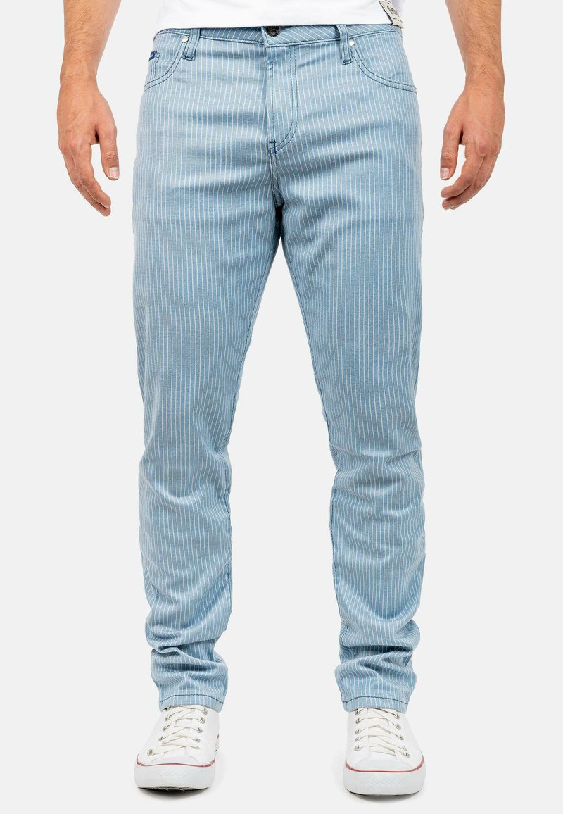 Lichtblauwe gestreepte jeans met een slim fit ontwerp, voorzien van een ritssluiting, vijf zakken en witte stiksels. Gepaarde met witte sneakers.