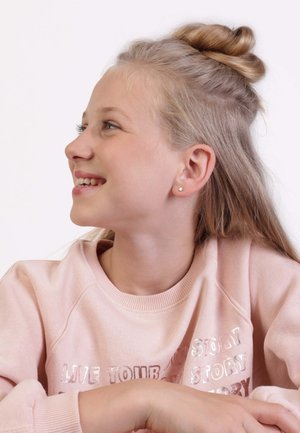 Sweatshirt rose clair avec un texte brillant, présentant un col rond et des manches raglan. Cheveux blonds longs coiffés en demi-queue, petites boucles d'oreilles en or.