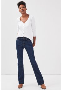 Valkoinen teksturoitu neuletakki, jossa on kolmivartiset hihat, nappikiinnitys. Yhdistetty tummansinisien leveälahkeisten farkkujen ja ruskeiden nilkkureiden kanssa.