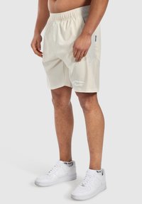 Krämfärgade träningsshorts med elastisk midja, sidopanel i nät och logotypdetalj. Matchas med vita sneakers.