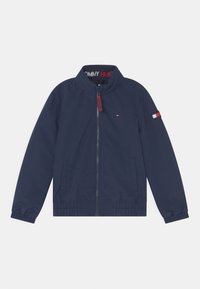 Marineblauwe windbreaker met opstaande kraag, volledige rits, elastische manchetten, twee zijzakken en logo-accenten op de mouw en rits.
