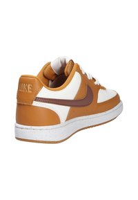 Baskets pour hommes avec tige en cuir marron et blanc, lacets texturés, col matelassé et semelle en caoutchouc blanche mouchetée. Marquage Nike au niveau du talon.