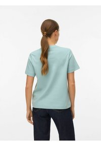 Lyseblå kortærmet t-shirt med rund hals og glat tekstur, kombineret med mørkeblå jeans med synlige stikninger på baglommerne.