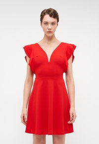 Robe rouge en tissu lisse, dotée d'un décolleté en V profond, de manches courtes à volants et d'un corsage ajusté qui s'évase à la taille.