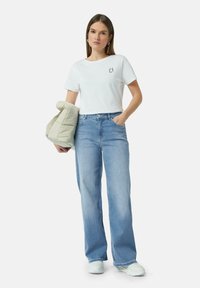 Witte T-shirt met korte mouwen en "C1" logo, gecombineerd met lichtblauwe wijde jeans en een beige pufferjack. Model draagt witte sneakers.