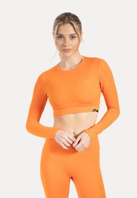 Oranje crop top met lange mouwen, gemaakt van gladde, rekbare stof. Heeft een ronde halslijn en een aansluitend ontwerp, gecombineerd met bijpassende leggings.