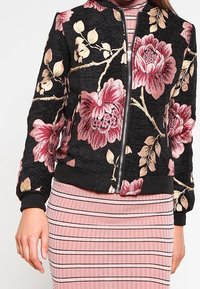 Černá bomber bunda s růžovou květinovou výšivkou, předním zipem a žebrovanými manžetami. Kombinováno s růžovými pruhovanými šaty.