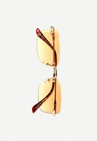 Béžové slnečné okuliare s zlatými kovovými akcentmi, štvorcovými šošovkami a hnedými vzorovanými stranami. Obsahujú nastaviteľné nosné podložky a detail loga.