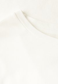 Bílá bavlněná trička s kulatým výstřihem. Hladká textura, jemná tkanina. Obsahuje mírně překrývající se vrstvy bez výrazných vzorů nebo akcentů.
